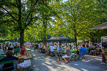 Ein gut besuchter Biergarten im Schatten der Bäume.